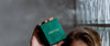 Loretana model holding branded green jewelry box high against glass block wall, complete sterling silver gift guide. Hand-finished Kaunas.