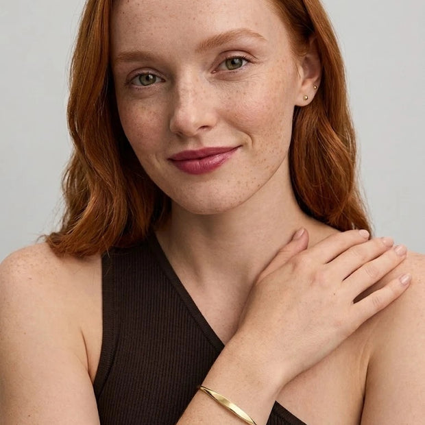 Smiling woman with her hand on her shoulder wearing the Personalized Letter Bangle in 18K gold-plated 925 silver