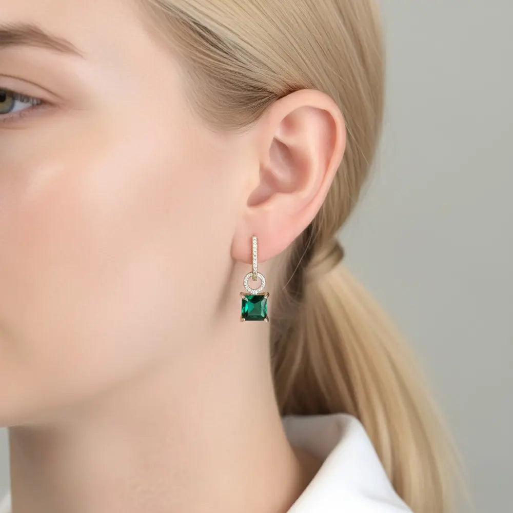 A profile lifestyle photograph of a woman wearing the 14K Gold Interchangeable Hoop earrings with the brilliant AAAAA emerald-green zirconia drop pendant attached, showcasing a sophisticated and vibrant botanical look for the modern ear stack.
