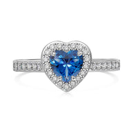 Hand model wearing the blue heart zirconia ring in 925 sterling silver with rhodium plating, deep blue stone resting flush against the finger in soft daylight. Hallmarked Loretana piece, hand-finished in Kaunas.